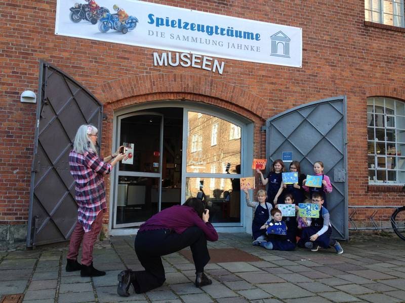 Eine Schulklasse vor dem Eingang der Museen, ein Kind zeigt ein Buch.