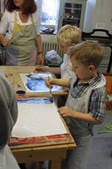 Kinder gestalten an einem Tisch Papier mit blauer Farbe.