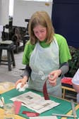 Ein Mädchen in Schürze klebt an einem Tisch Papier zusammen.