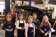 Eine Gruppe Kinder in Schürzen steht vor den Druckmaschinen.